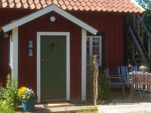 A red building with a green door, a small window, and a porch with chairs. - 6 Person Holiday Home in Stjarnhov (Stjarnhov)