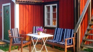 A wooden deck with two striped chairs and a table, a red building with a window, and a wooden staircase. - 6 Person Holiday Home in Stjarnhov (Stjarnhov)