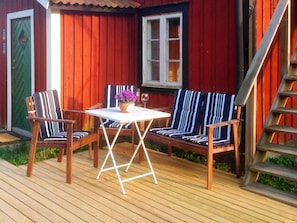 A wooden deck with two striped chairs and a table, a red building with a window, and a wooden staircase. - 6 Person Holiday Home in Stjarnhov (Stjarnhov)