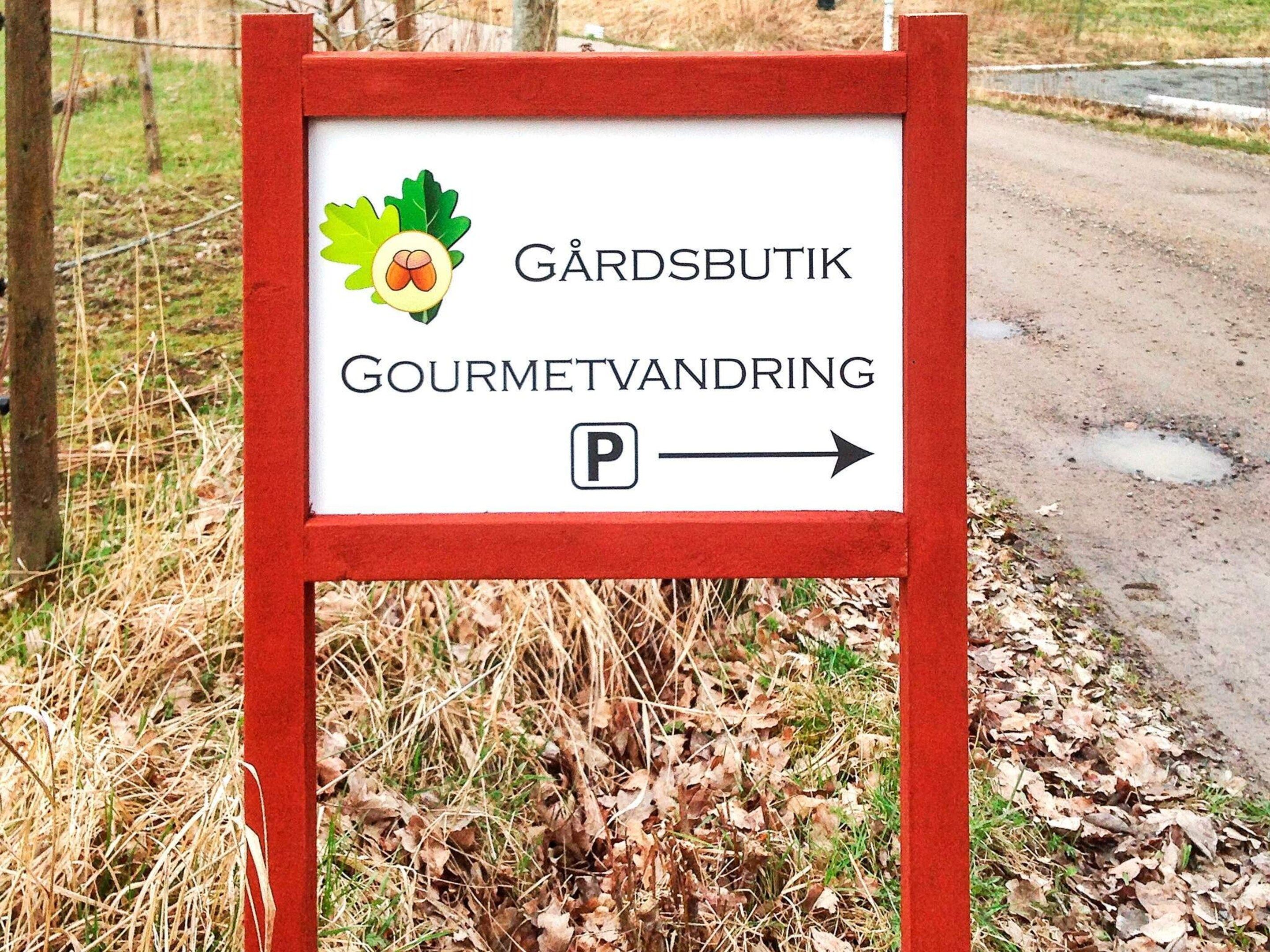 A sign with a parking symbol and text indicating a direction to a place called 'GÄRDSBUTIK' and 'GOURMETVANDRING'.