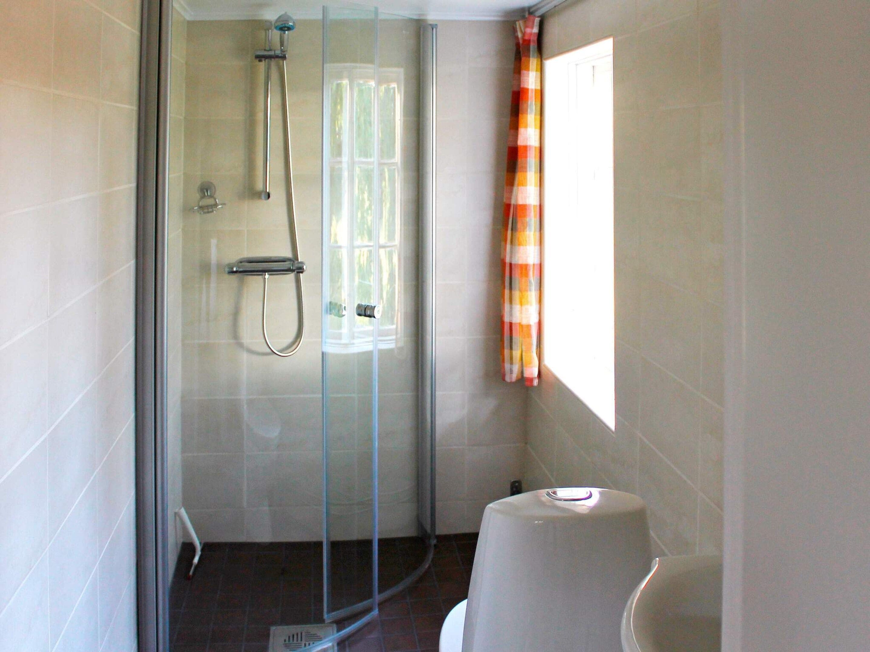 A bathroom with a glass-enclosed shower, a toilet, and a window with a curtain.
