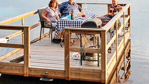 A wooden dock with a table and chairs, a grill, and a small boat. - 6 Person Holiday Home in Stjarnhov (Stjarnhov)