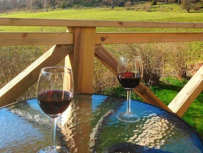 A glass table with two wine glasses on it, set against a wooden railing with a view of a grassy field. - 6 Person Holiday Home in Stjarnhov (Stjarnhov)