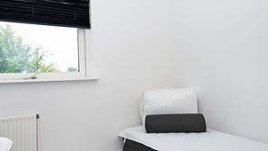 A small, single-bed room with a window, a radiator, and a plain white wall.