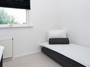 A small, single-bed room with a window, a radiator, and a plain white wall.