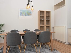 Ein Essbereich mit Holztisch, grauen Stühlen, einem Schrank mit Gläsern und einem gerahmten abstrakten Gemälde an der Wand.