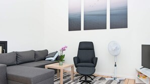 A modern living room with a grey sectional sofa, a black office chair, a small table with a plant, and a large flat-screen TV.