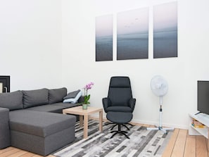 A modern living room with a grey sectional sofa, a black office chair, a small table with a plant, and a large flat-screen TV.