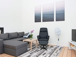 Una sala moderna con un sofá seccional gris, una silla de oficina negra, una mesita con una planta y un televisor de pantalla plana grande.