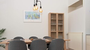 A dining area with a wooden table, grey upholstered chairs, a cabinet with glassware, and a framed abstract painting on the wall.