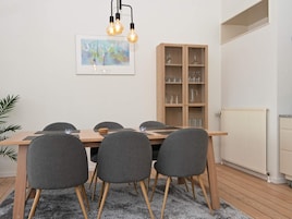 Un comedor con una mesa de madera, sillas tapizadas de gris, un armario con cristalería y un cuadro abstracto enmarcado en la pared.