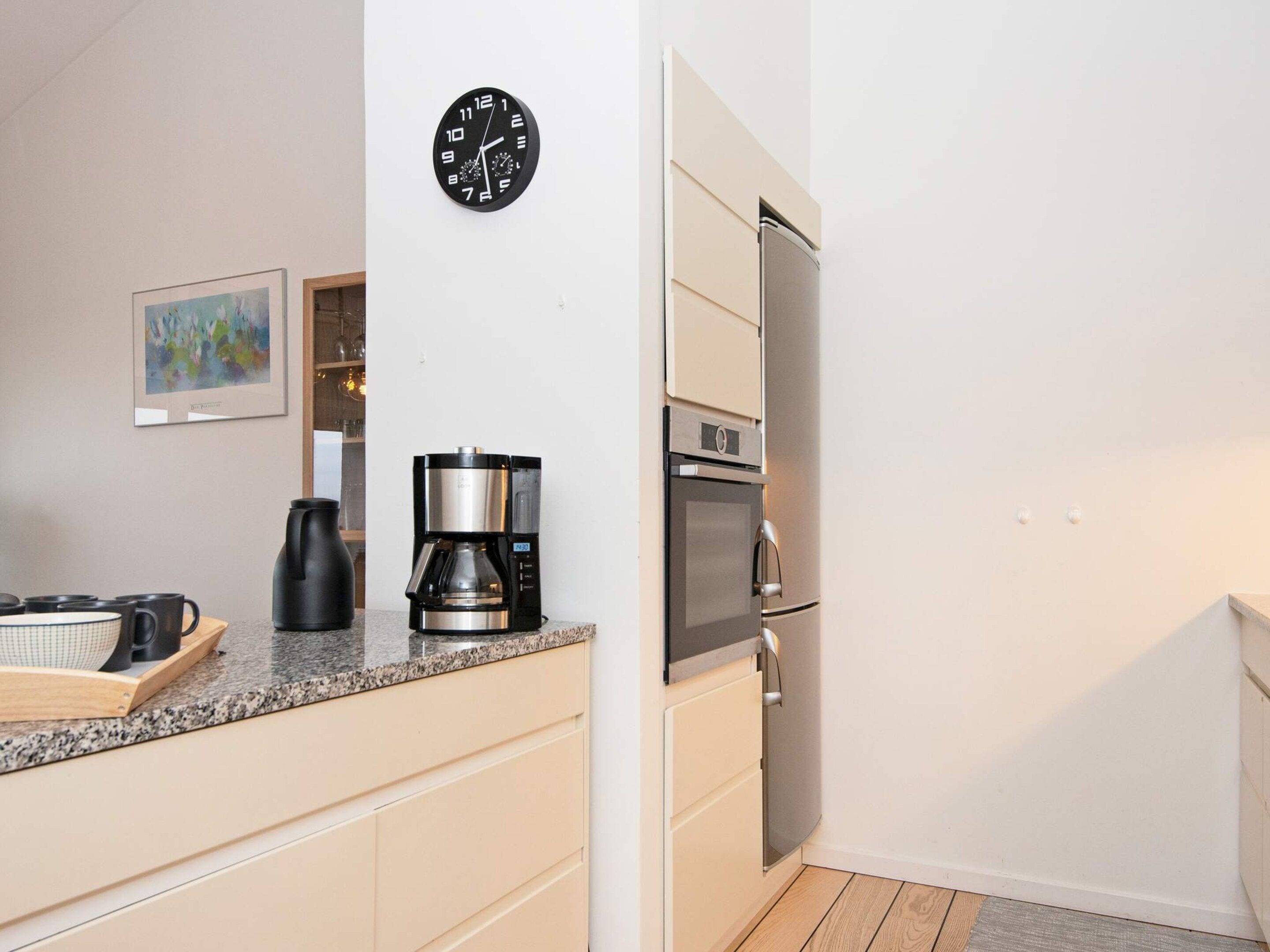 A compact kitchen with a coffee maker, a clock, and a refrigerator.