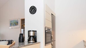A compact kitchen with a coffee maker, a clock, and a refrigerator.
