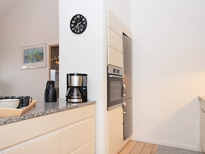 A compact kitchen with a coffee maker, a clock, and a refrigerator.