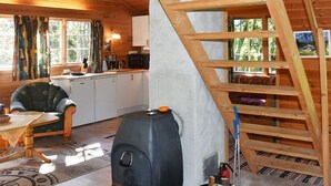 A cozy cabin interior with a wood stove, a dining area, and a staircase leading to an upper level.