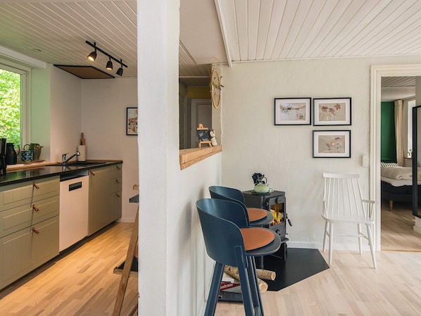 A modern kitchen with wooden cabinets, a black countertop, and a built-in stove. There are two blue chairs and a white table in the adjacent dining area.
