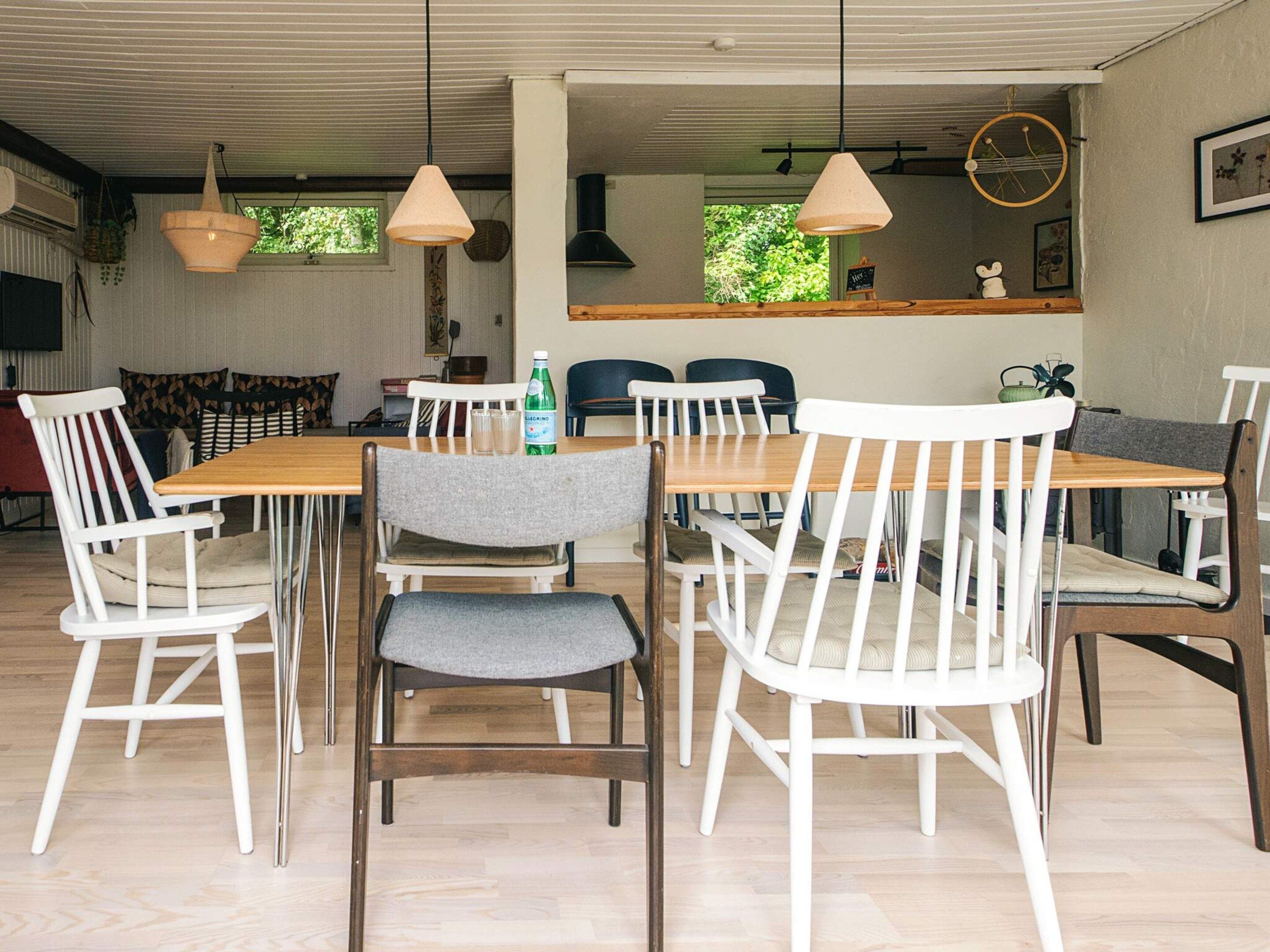 Un comedor con mesa de madera y sillas blancas, una botella de agua y una lámpara colgante.