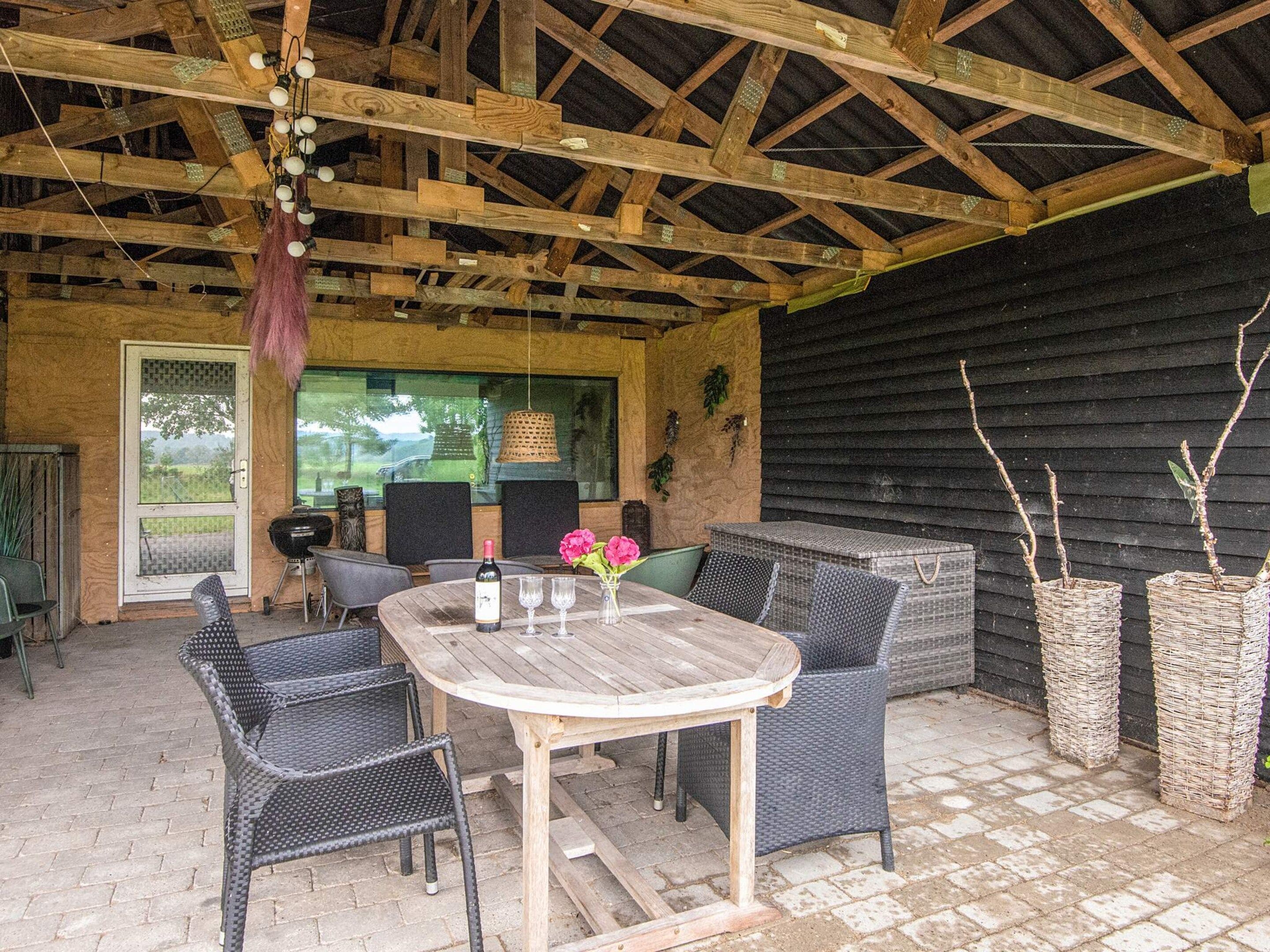 An outdoor patio with a wooden table and wicker chairs, a grill, and potted plants.
