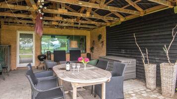 An outdoor patio with a wooden table and wicker chairs, a grill, and potted plants.