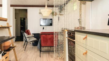 A modern kitchen with a built-in oven, a dining area with a red chair, and a hanging light fixture.
