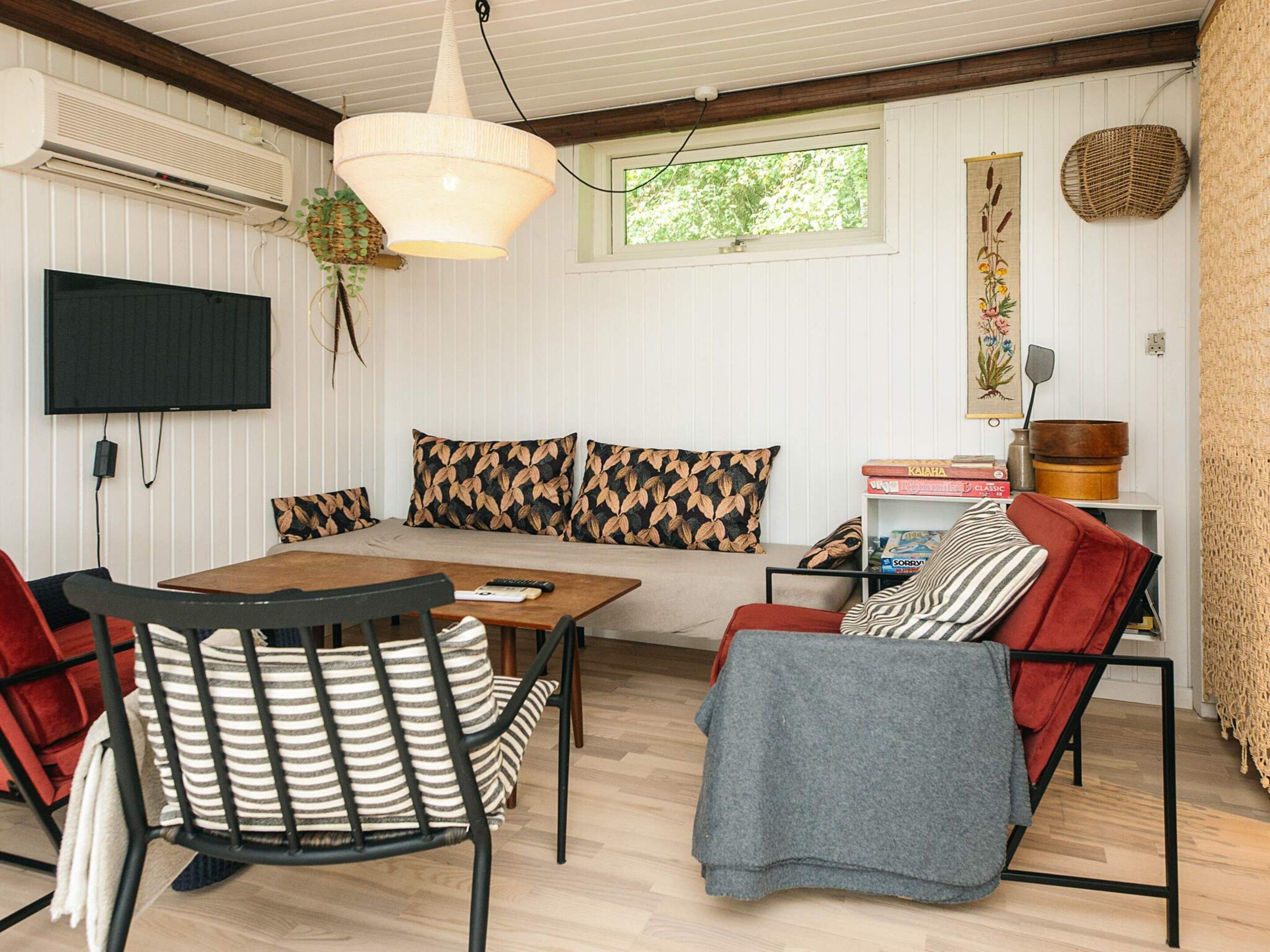 Una sala de estar acogedora con un sofá, una mesa de comedor y sillas. Hay un televisor montado en la pared, una lámpara colgante y una ventana con vistas a zonas verdes.