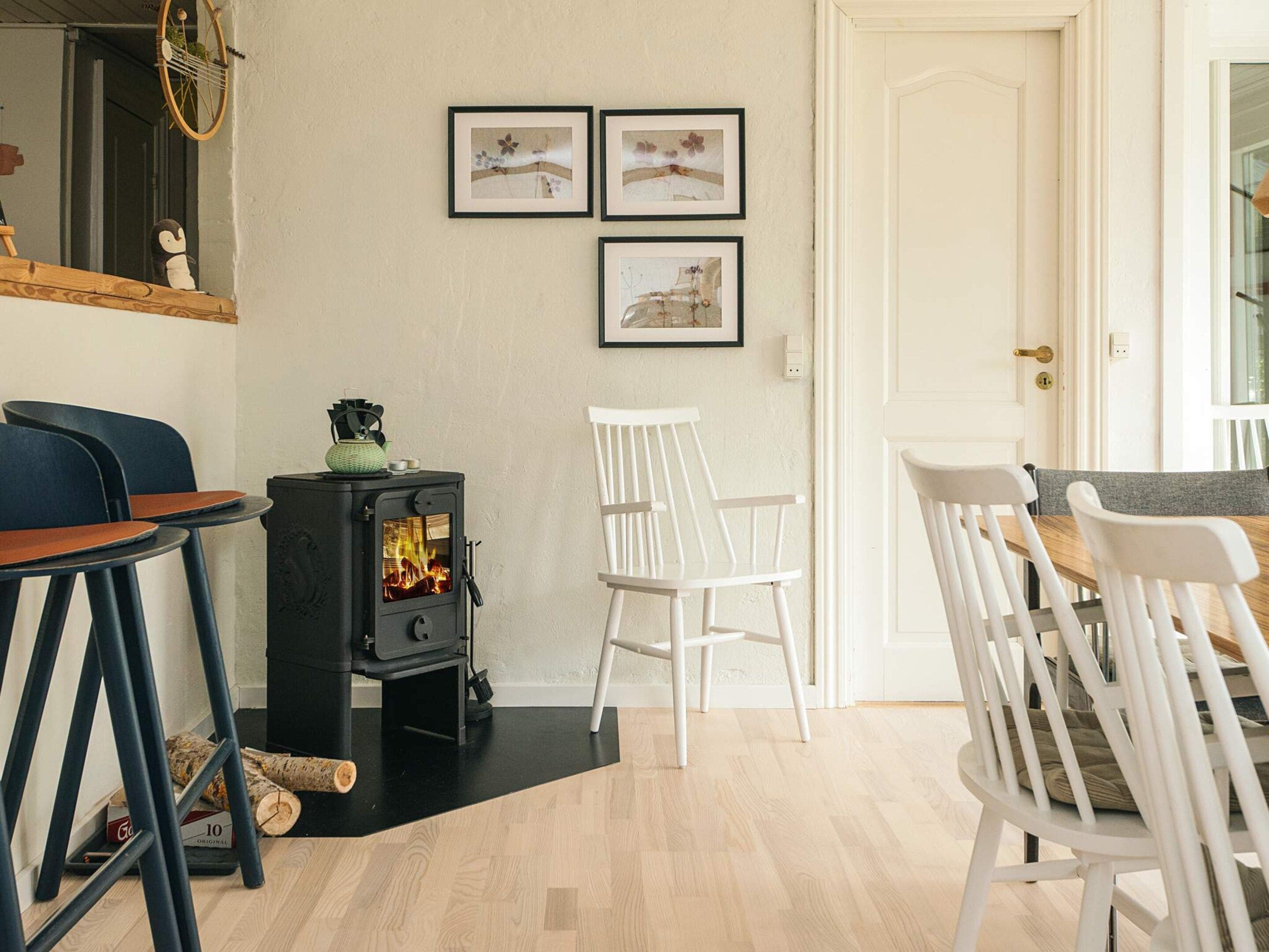 A cozy room with a wood-burning stove, white chairs, and framed pictures on the wall.