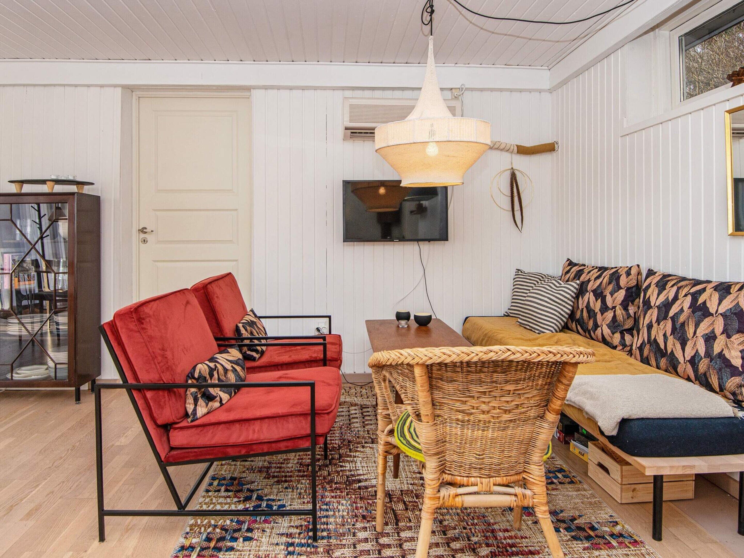 A cozy living room with a red sofa, a wicker chair, a wooden table, and a television mounted on the wall.