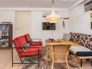 Un salon chaleureux avec un canapé rouge, un fauteuil en osier, une table en bois et un téléviseur fixé au mur.