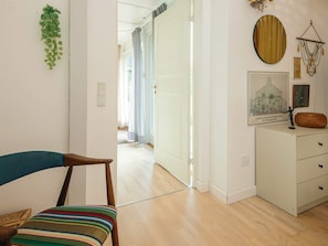 A room with a wooden floor, a white cabinet with drawers, a chair with a striped cushion, a hanging plant, and a framed picture on the wall.