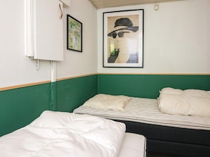 A room with two beds, one with a green headboard and the other with a dark headboard. There is a framed picture on the wall above the beds.