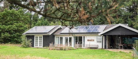 Uma casa com telhado inclinado, painéis solares e varanda coberta.