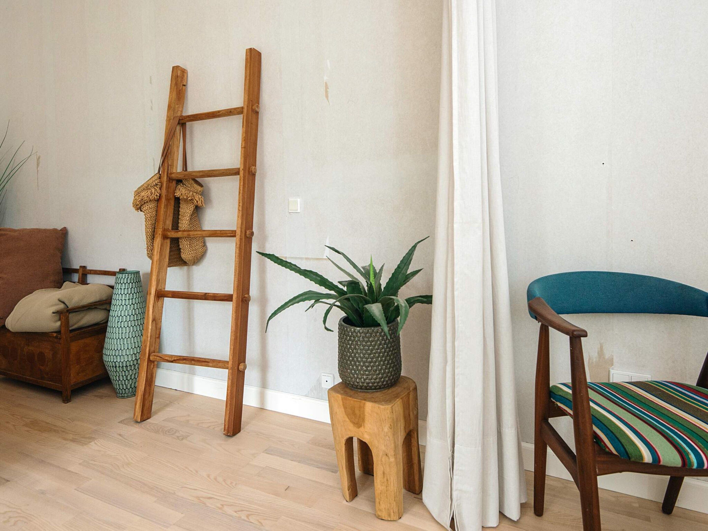 A room with a wooden ladder, a potted plant, a striped chair, and a wooden stool.