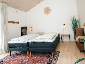 Une chambre à coucher avec un lit double, deux tables de chevet, une lampe sur pied, une chaise, une plante en pot et un tapis à motifs.