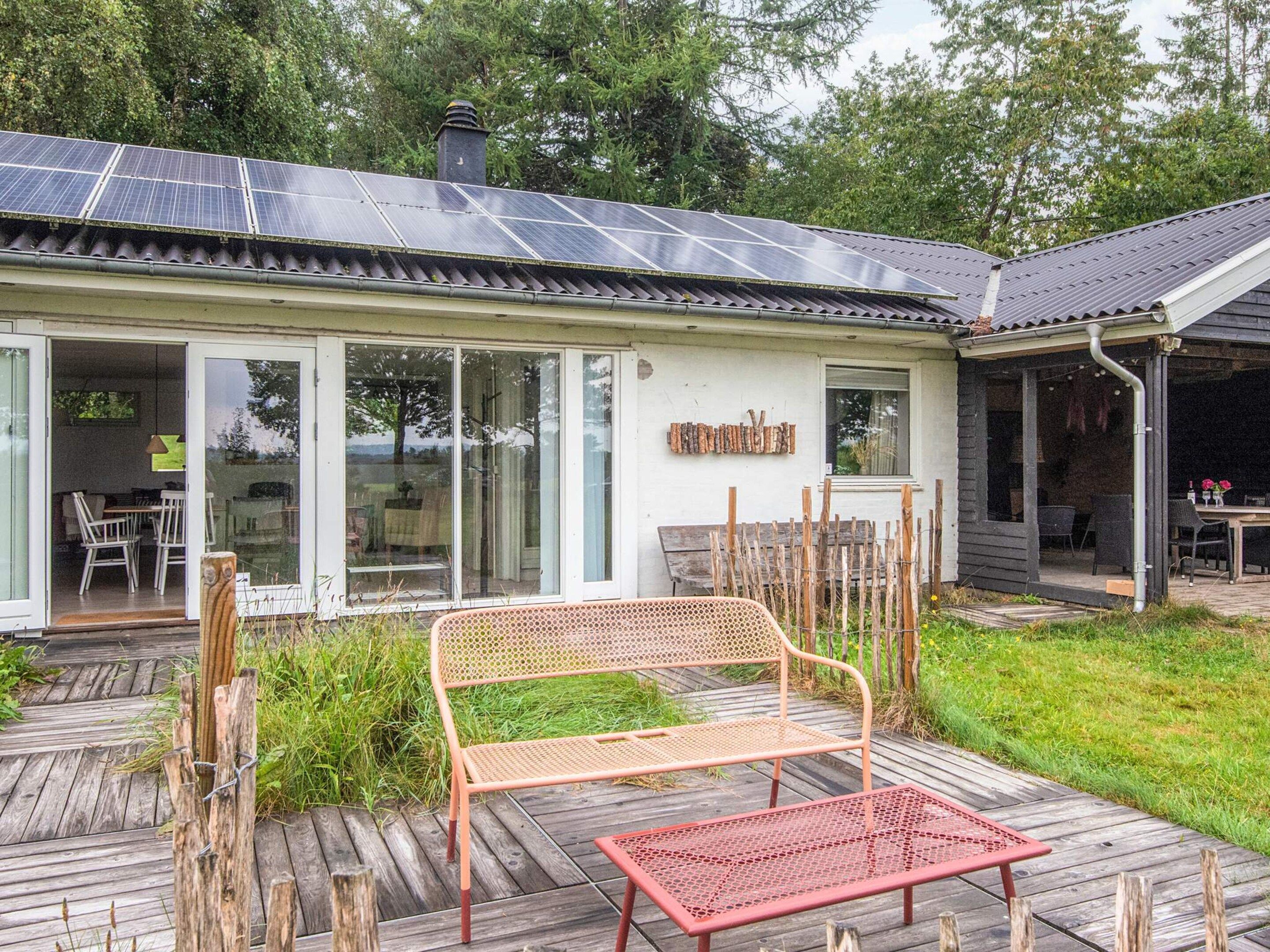A house with a solar panel roof, a covered patio with a bench, and a wooden deck.