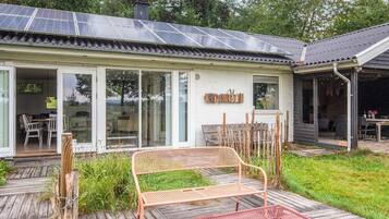 A house with a solar panel roof, a covered patio with a bench, and a wooden deck.