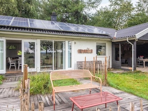 Une maison avec un toit équipé de panneaux solaires, un patio couvert avec un banc et une terrasse en bois.