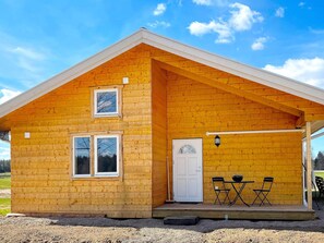 A wooden cabin with a gabled roof, a front door, and a small porch with a table and chairs. - 4 Star Holiday Home in Sandhem (Sandhem)