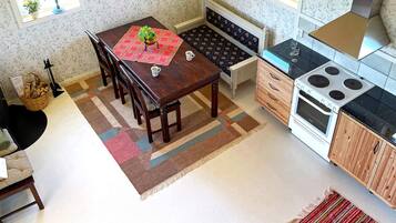 Uma cozinha com uma mesa de jantar, cadeiras, fogão e uma pequena janela com uma planta.