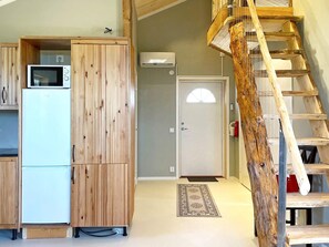 A compact kitchen with wooden cabinetry, a white refrigerator, and a microwave. A wooden staircase with a metal railing leads to a door with a small window. - 4 Star Holiday Home in Sandhem (Sandhem)