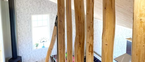 A room with a wooden ceiling, a fireplace, a window, and a stove.