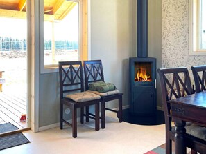 A room with a built-in wood-burning stove, wooden chairs with cushions, and a view through a window.