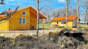 Une maison en bois jaune avec un toit rouge, une véranda et un mur de pierre au premier plan.