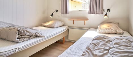 A room with two beds, a window with curtains, and wall-mounted lamps.