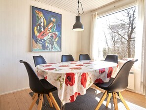 A dining area with a round table, black chairs, a floral tablecloth, a hanging light, and a large abstract painting on the wall. - 6 Person Holiday Home in Aakirkeby (Akirkeby)