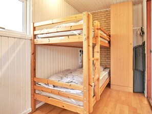 A bunk bed with a wooden frame, a brick wall behind, and a door to the right.