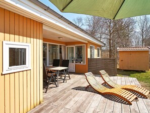 A wooden deck with a table and chairs, a covered patio area, and a shed in the background.
