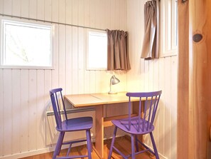 Quarto com escrivaninha de madeira, duas cadeiras roxas, luminária e janela com cortinas.