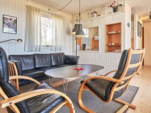A modern living room with a leather sofa, wooden chairs, a round table, and a hanging light fixture.