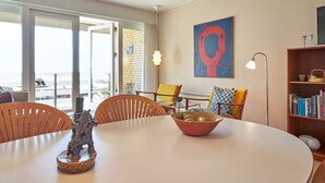 Ein modernes Wohnzimmer mit einem runden Tisch, Stühlen, einem Bücherregal und einem großen Fenster mit Blick.