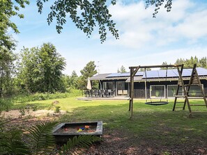 A residential property with a patio area, outdoor seating, a swing set, and a solar panel roof.